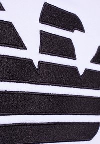 Black embroidered logo with geometric shapes and stripes on a white fabric background, emphasizing texture and contrast.