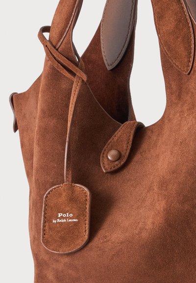 Sac à main Polo en daim marron de Ralph Lauren avec des détails en cuir et une sangle boutonnée sur un fond uni.