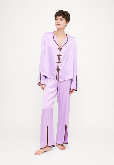 Ensemble de loungewear satin lavande composé d'un haut à manches longues avec des bordures marron et des fermetures à lacet, associé à un pantalon large assorti.