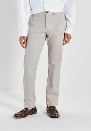 Helle beige Hosen aus strukturiertem Stoff, mit geradem Schnitt und vorderen Taschen, kombiniert mit dunkelbraunen Slippern mit goldfarbenen Beschlägen.