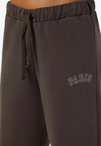 Tummanharmaat collegehousut, joissa on joustava vyötärö, naru ja vasemmassa reidessä valkoiset tekstit "PARIISI". Pehmeä kangas ja rento malli.