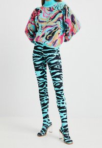 Multifarvet, blød pullover med blå, pink og sorte hvirvler; kombineret med sorte og turkis tigerstribede leggings; gennemsigtige sandaletter med h�æl.