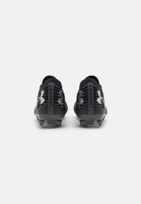 Scarpe da calcio nere con un'estremità testurizzata, caratterizzate da dettagli argentati, logo Under Armour e tacchetti conici per la trazione.