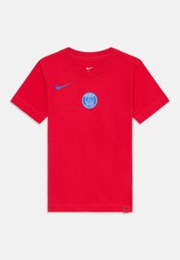 T-shirt en coton rouge avec un col rond, arborant un logo Nike bleu sur la poitrine gauche et un emblème circulaire bleu du Paris Saint-Germain.