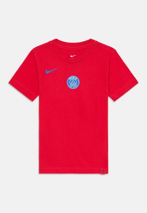 T-shirt en coton rouge avec un col rond, arborant un logo Nike bleu sur la poitrine gauche et un emblème circulaire bleu du Paris Saint-Germain.