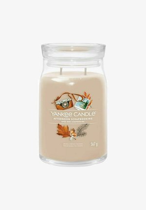 Yankee Candle i en klar glasbeholder. Crèmefarvet voks med to væger. Etiketten viser efterårs-tema grafik og læser "Eftermiddag Scrapbooking."