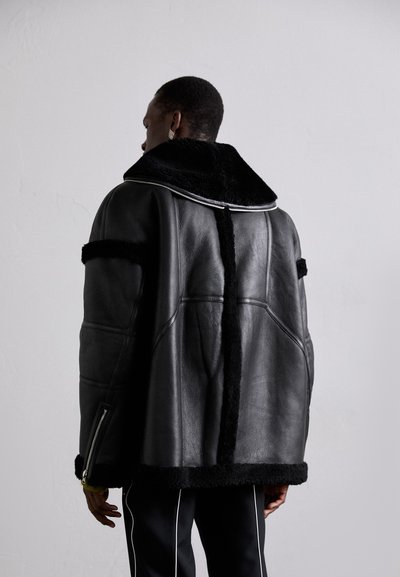 Black leather jacket with a faux fur collar, featuring angular design, side zippers, and a contrasting black shearling trim along the hem.