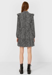 Vestido de leopardo en blanco y negro con hombros con volantes, mangas largas y falda de capas. Combinado con botas de tobillo negras y gruesas.
