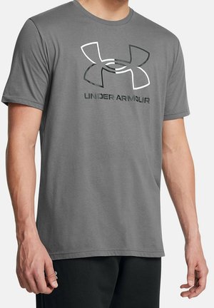 Mand iført en grå Under Armour t-shirt med logo og tekst foran, kombineret med sorte bukser.