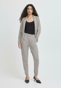 Šedý, upravený oblek s texturovaným propletením, kombinovaný s černým topem na ramínka. Slim-fit kalhoty se bočními kapsami a odpovídajícím sakem. Černé lodičky.