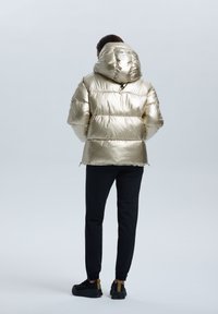 Metallisk guld puffjacka med huva, med kviltade sektioner och en slät yta. Kombinerad med svarta tapered byxor och mörka sneakers.