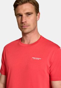 Tricou roșu din bumbac, cu guler rotund, mâneci scurte și un mic logo alb pe partea stângă a pieptului, conceput pentru un aspect ajustat.
