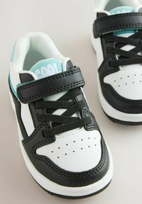 Zwart-witte sneakers met een glad leren afwerking, voorzien van een gewatteerde kraag, geperforeerde neus en teal accenten. Klittenbandsluiting en veters.