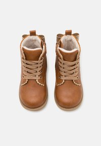 Bottes ankle en cuir marron avec une finition texturée, des bords festonnés et des lacets dorés, dotées d'une doublure intérieure douce et d'un talon renforcé.
