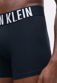 Fekete pamut boxer alsónadrág feh�ér "Calvin Klein" logóval az elasztikus derékpánton; illeszkedő dizájn sima textúrával.
