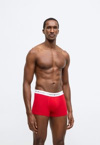 Røde boxershorts i bomuld med en hvid linning, der har teksten "TOMMY HILFIGER". Designet er tætsiddende og har en glat tekstur.