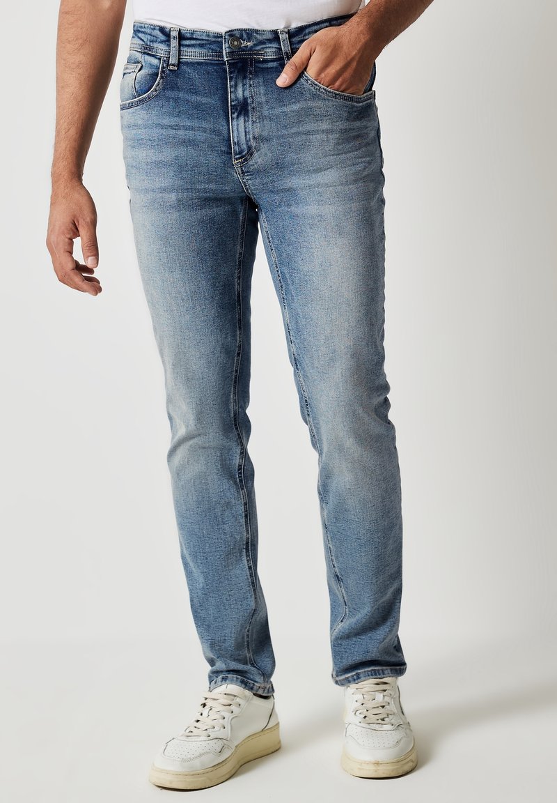 Vaaleansinset farkut slim fit -mallilla, joissa on nappi- ja vetskariolka, vyölenkit ja etutaskut, joita on käytetty valkoisten tennareiden kanssa.