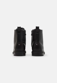 Bottines en cuir noir avec une finition texturée, fermeture éclaire et petit accent logo au talon. Semelle lisse et forme arrondie.