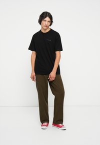 Camiseta de algodón negra de manga corta y cuello redondo, combinada con pantalones de pana verde oscuro y zapatillas rojas. Diseño simple.