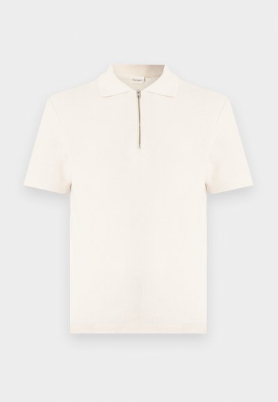 Λευκό πόλο με κοντά μανίκια και υφή, με γιακά και κλείσιμο με φερμουάρ μπροστά, παρουσιάζεται σε απλό φόντο.