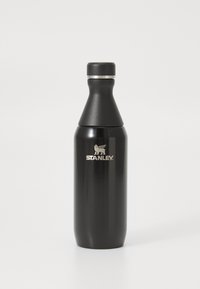 Bouteille d'eau en acier inoxydable noir avec une forme effilée, une bande d'accent argentée et le logo "STANLEY" en blanc près de la base.