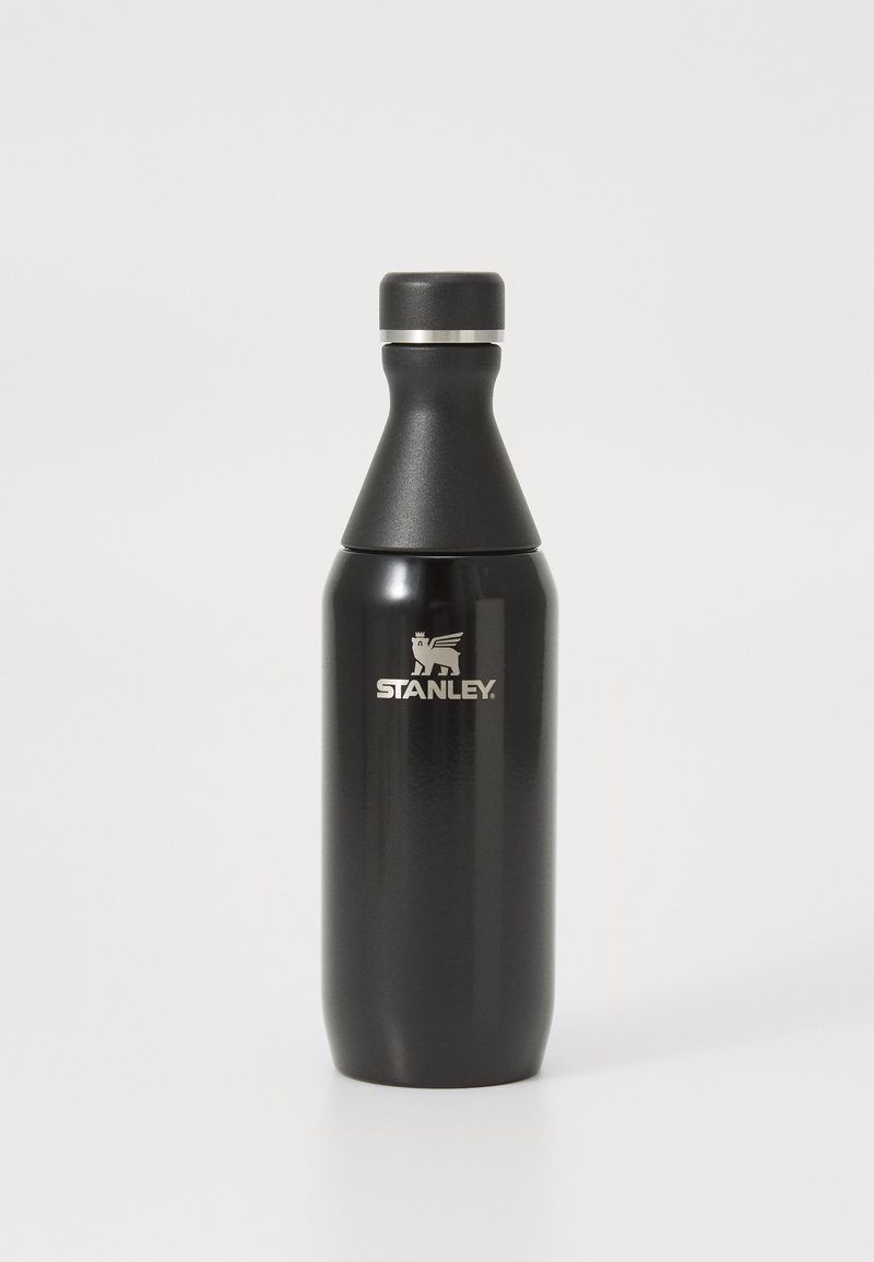 Bouteille d'eau en acier inoxydable noir avec une forme effilée, une bande d'accent argentée et le logo "STANLEY" en blanc près de la base.