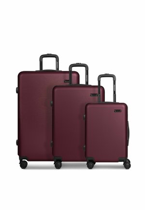 Trois valises rigides couleur marron foncé avec des poignées et des roues noires, disposées par taille décroissante sur un fond blanc.