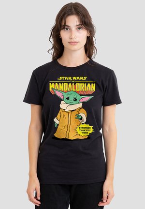 Schwarzes T-Shirt mit einem grafischen Motiv eines grünen Charakters in einem braunen Mantel, mit dem Text "Stärker als du denkst" in Gelb und roten Akzenten.