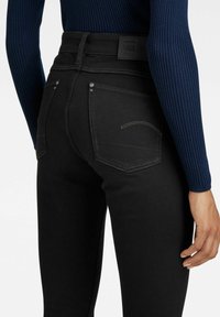 Svarta denimjeans med hög midja, med en slät textur, kontrasterande sömdetaljer och två bakfickor.
