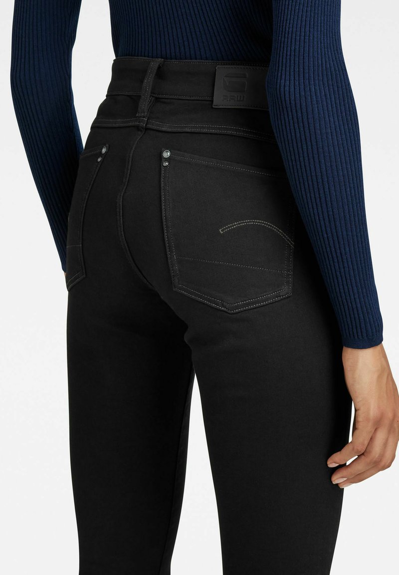 Schwarze Denim-Jeans mit hoher Taille, ausgestattet mit einer glatten Textur, kontrastierenden Nähdetails und zwei Gesäßtaschen.