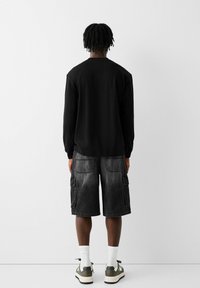 Camisa negra de manga larga combinada con pantalones cortos cargo grises que cuentan con múltiples bolsillos, finalizada con calcetines blancos y calzado oscuro.