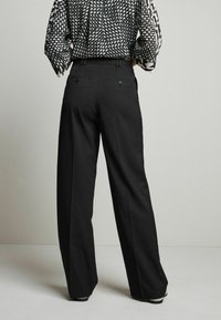 Black wide-leg trousers with a smooth texture, featuring dual back pockets and a tailored fit. Worn with a patterned top.