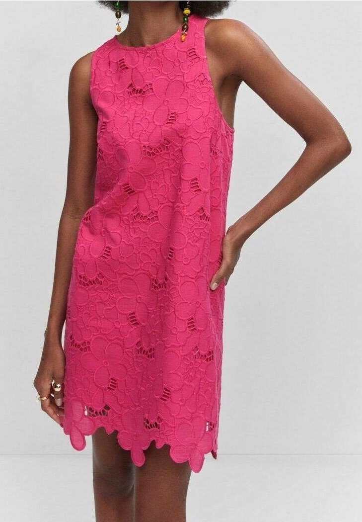 Robe sans manches en dentelle rose vif avec de grands motifs floraux et un ourlet festonné portée par une personne avec une main sur la hanche.