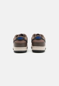 Nike tenisky hnedé s čiernymi akcentmi; hladký kožený zvršok, polstrovaný golier, modré logo na päte a textúrovaná gumová podrážka.