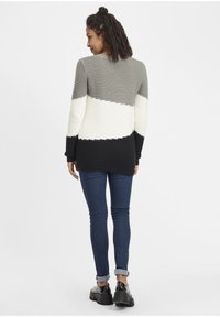 Strikket cardigan i grå, hvit og svart. Har et teksturert mønster, løs passform og lange ermer. Kombinert med mørk denim og kraftige sko.