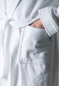 White terry bathrobe with a waist tie, featuring a textured surface, ribbed cuffs, and side pockets. Soft and absorbent fabric.