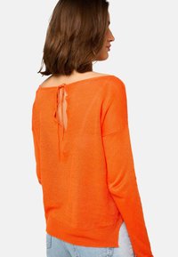 Pull orange à coupe ample, décolleté large et détail en forme de trou de serrure au dos, fabriqué dans un matériau doux et léger.