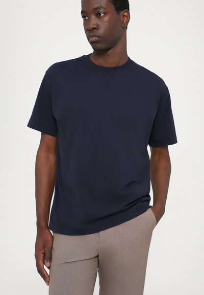 T-shirt en coton bleu marine à manches courtes, col rond et coupe décontractée, associé à un pantalon taillé marron clair.