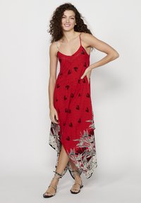 Robe rouge sans manches avec un motif géométrique, des accents noirs et un ourlet flottant avec un design floral à la base.
