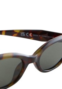 Brilles ar pūķa čaumalas rakstu un zaļgandzeltenām pārejām lēcām. Apaļa ietvara dizains. Acetāta materiāls ar dzelteniem akcentiem. Redzama uzlīme "Izgatavots Ķīnā".