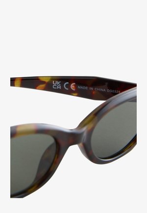 Sausumos akiniai nuo saulės su gradientinėmis žaliomis lęšiais. Apvalus rėmo dizainas. Acetato medžiaga su geltonais akcentais. Matomas etiketės užrašas „Pagaminta Kinijoje“.