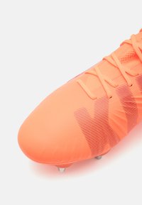 Scarpino da calcio arancione brillante con una tomaia liscia e testurizzata, lacci sottili e un motivo decorativo. Presenta tacchetti metallici sulla suola.