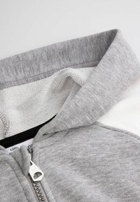 Szary hoodie zapinany na zamek, charakteryzujący się miękką, teksturowaną powierzchnią i kontrastującym białym wnętrzem. Posiada metalowy zamek błyskawiczny oraz kaptur.