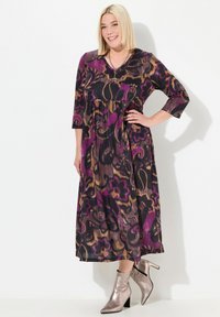 Robe maxi avec un décolleté en V, des manches trois quarts, des motifs floraux et abstraits en violet, noir et or, accompagnée de bottines métalliques.
