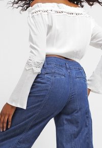 Top bianco scollato con dettagli in pizzo alle maniche abbinato a jeans in denim a vita alta in un lavaggio blu scuro.