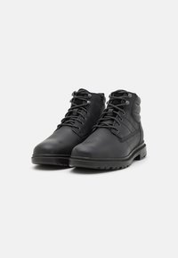 Botas de cuero negro hasta el tobillo con puntera redondeada, cuello acolchado, diseño de cordones y lengüeta texturizada. Suela de goma con detalles de tracción.