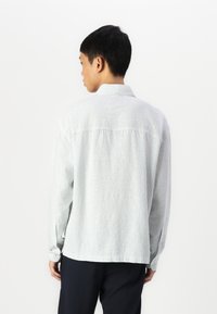 Camisa de botões de riscas azul claro e branca, com mangas longas, colarinho clássico e um corte ligeiramente relaxado.