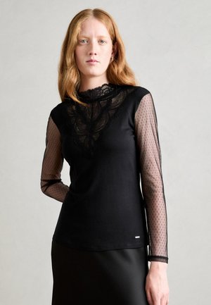 Chemise noire à manches longues avec un corps uni, des manches en dentelle et en mesh à pois, un décolleté festonné et une silhouette ajustée.