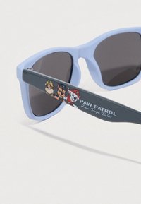 Jasnoniebieskie okulary przeciwsłoneczne z ciemnymi szkłami mają ciemnoszare zauszniki ozdobione postaciami z Psiego Patrolu oraz napisem „Paw Patrol These Pups Rock!”