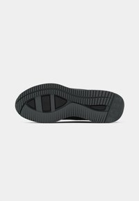 Semelle de chaussure de sport noire avec un motif texturé. Présente un design incurvé, des zones en retrait, ainsi que des rainures horizontales et verticales pour une meilleure adhérence.